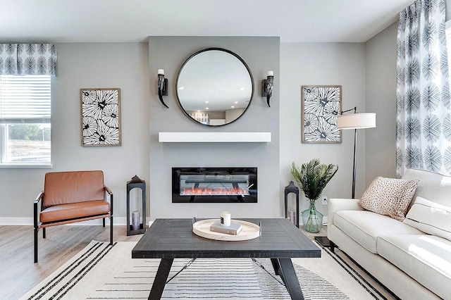 living area with a glass covered fireplace, wood finished floors, and baseboards