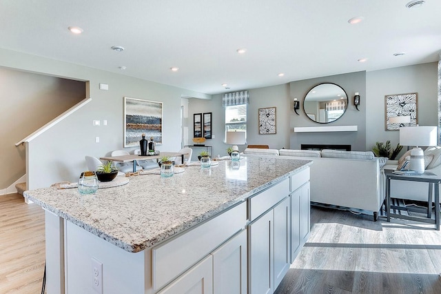kitchen with recessed lighting, light stone counters, light wood-type flooring, a kitchen island, and open floor plan