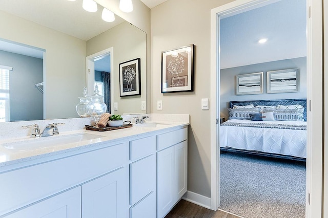 ensuite bathroom featuring baseboards, wood finished floors, a sink, and double vanity