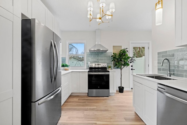 kitchen with backsplash, a sink, wall chimney exhaust hood, light wood-style flooring, and appliances with stainless steel finishes