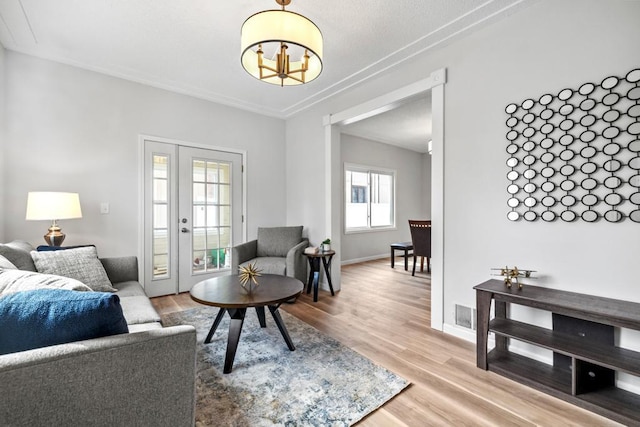 living room with light wood-type flooring, visible vents, baseboards, and an inviting chandelier