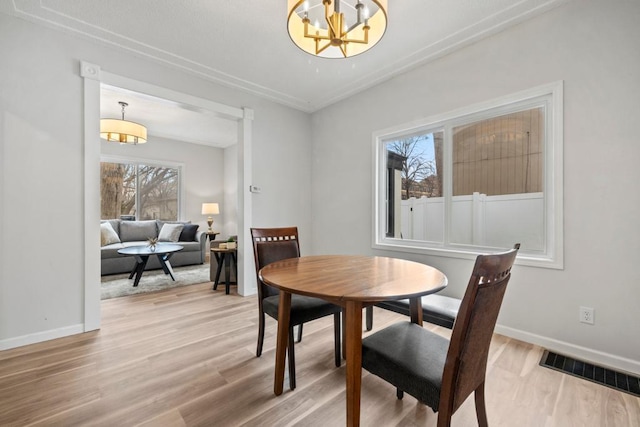 dining space with light wood finished floors, baseboards, visible vents, and a chandelier