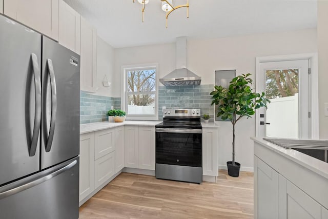 kitchen featuring wall chimney range hood, white cabinetry, stainless steel appliances, and light wood-type flooring