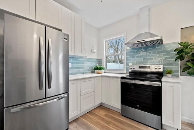 kitchen featuring white cabinets, stainless steel appliances, and wall chimney range hood