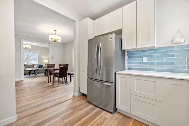 kitchen featuring decorative backsplash, light wood-style flooring, baseboards, white cabinetry, and freestanding refrigerator