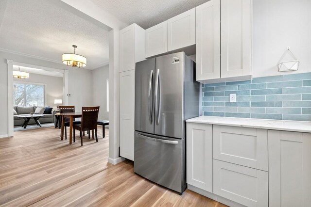 kitchen with backsplash, freestanding refrigerator, light wood finished floors, and white cabinetry
