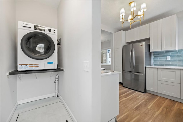 kitchen featuring baseboards, freestanding refrigerator, an inviting chandelier, decorative backsplash, and washer / dryer