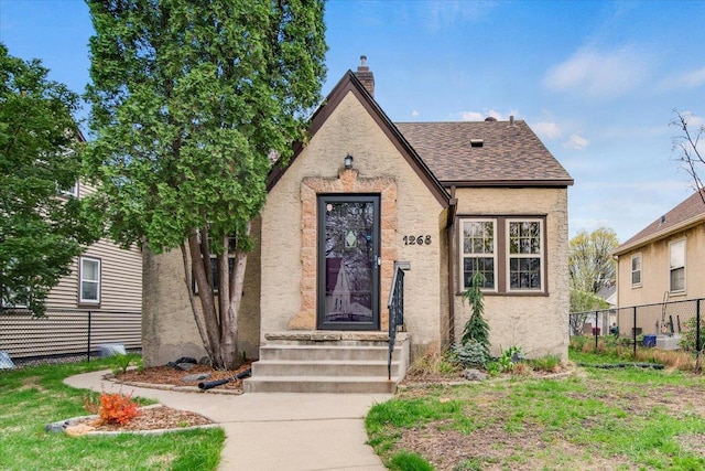tudor-style house with fence, a chimney, and stucco siding