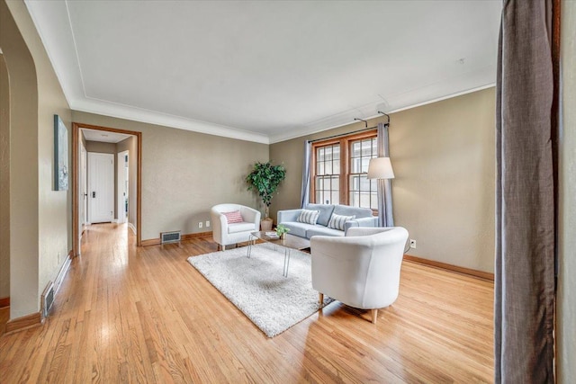 living room with crown molding, light wood-style floors, arched walkways, baseboards, and visible vents