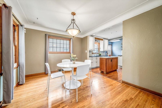 dining area with baseboards, a textured wall, and light wood-type flooring