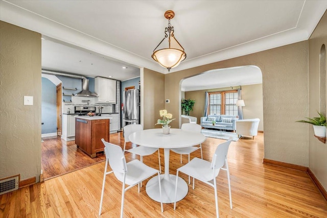 dining area with arched walkways, a textured wall, visible vents, and light wood finished floors