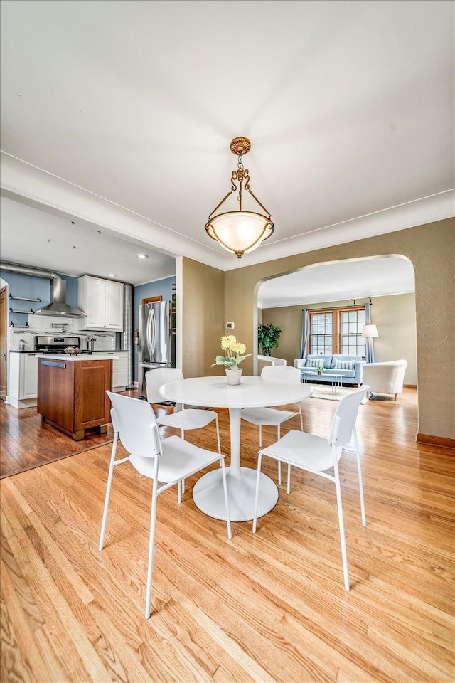 dining room featuring baseboards, arched walkways, and light wood-style flooring