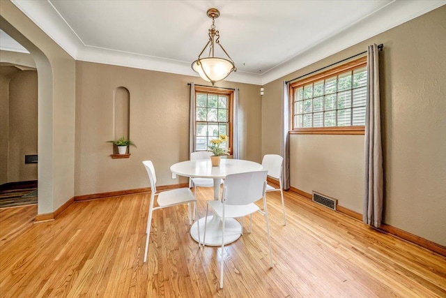 dining room with a healthy amount of sunlight, arched walkways, light wood finished floors, and visible vents