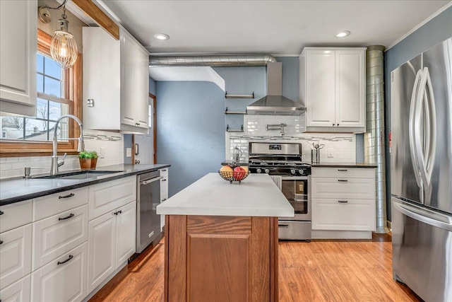 kitchen featuring wall chimney range hood, white cabinets, appliances with stainless steel finishes, a sink, and decorative backsplash