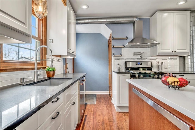 kitchen featuring appliances with stainless steel finishes, tasteful backsplash, white cabinetry, a sink, and wall chimney exhaust hood