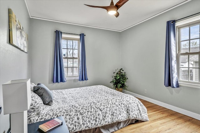 bedroom featuring baseboards, ceiling fan, wood finished floors, and multiple windows