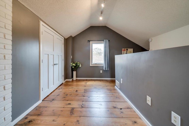 bonus room with baseboards, vaulted ceiling, light wood finished floors, and a textured ceiling