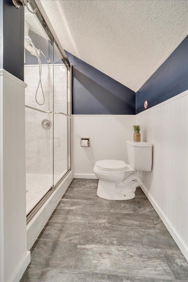 bathroom with a textured ceiling, a wainscoted wall, toilet, and a shower stall