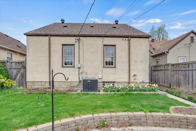 back of property featuring a fenced backyard, stucco siding, a yard, and central AC