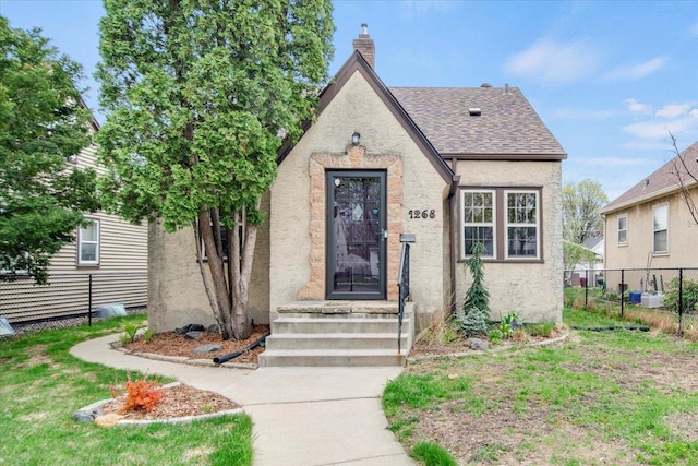 tudor home with fence, a chimney, and stucco siding