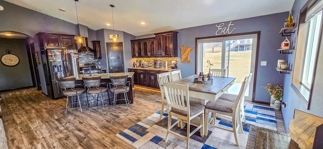 kitchen featuring stainless steel fridge with ice dispenser, tasteful backsplash, light countertops, wood finished floors, and vaulted ceiling