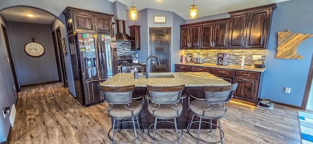 kitchen featuring an island with sink, light stone countertops, appliances with stainless steel finishes, wood finished floors, and a sink