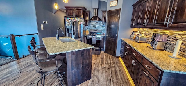kitchen featuring appliances with stainless steel finishes, an island with sink, light stone countertops, dark wood finished floors, and a sink
