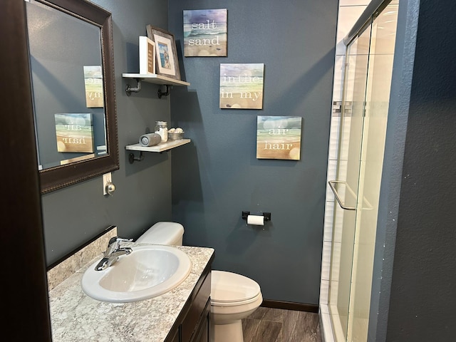 bathroom featuring baseboards, toilet, vanity, wood finished floors, and a stall shower