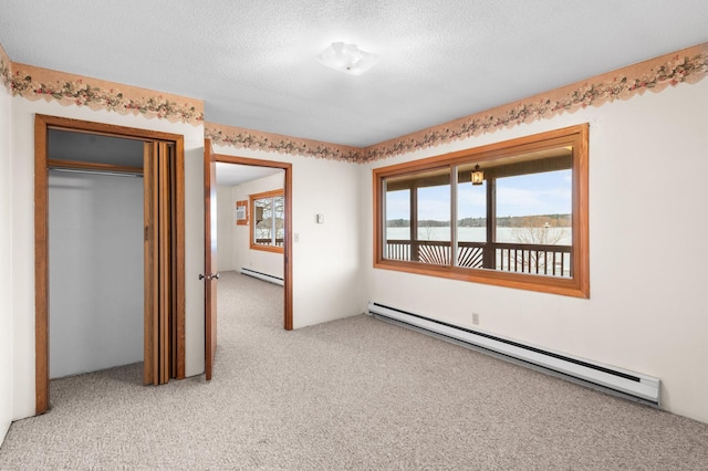 unfurnished room with a baseboard heating unit, a water view, a baseboard radiator, a textured ceiling, and light colored carpet