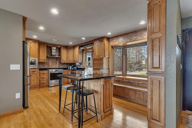 3202 Riviera Rd, Sartell, MN 56377 - kitchen featuring wall chimney range hood, light wood finished floors, a kitchen breakfast bar, stainless steel appliances, and recessed lighting
