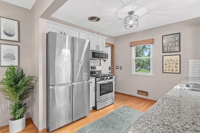 7244 12th Ave S, Richfield, MN 55423 - kitchen featuring stainless steel appliances, white cabinetry, light stone counters, and light wood-type flooring