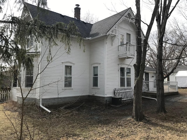 view of home's exterior with a balcony, a chimney, a shingled roof, and central AC unit