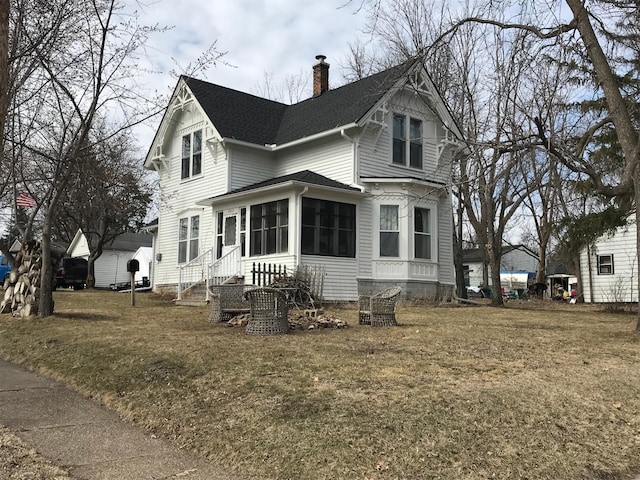 view of front of home featuring a chimney, a shingled roof, a sunroom, and a front lawn