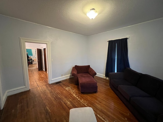 living room with wood finished floors, a textured ceiling, baseboards, and ornamental molding