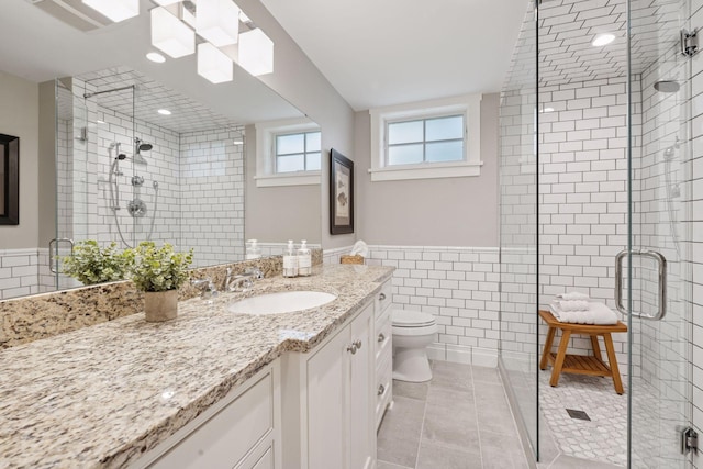 full bath with a stall shower, tile walls, vanity, and toilet