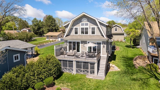 back of property featuring a gambrel roof, a sunroom, a wooden deck, and a lawn