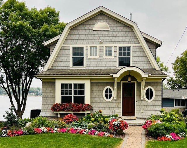 view of front of house featuring a gambrel roof, roof with shingles, and a front yard