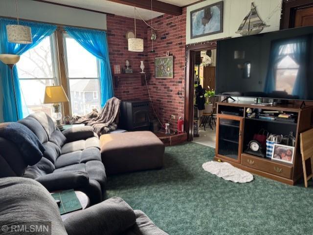 carpeted living area featuring a wood stove, beamed ceiling, and brick wall