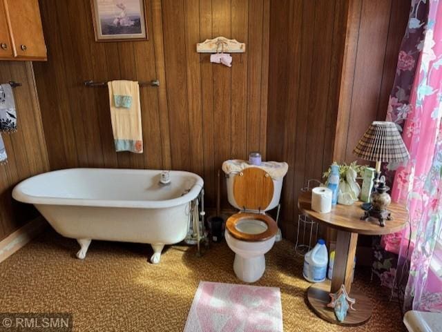 full bathroom featuring toilet, a freestanding tub, and wood walls