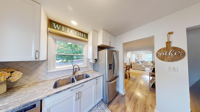 kitchen featuring light wood finished floors, stainless steel appliances, tasteful backsplash, white cabinetry, and a sink