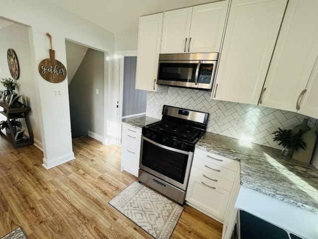 kitchen with white cabinetry, light stone countertops, light wood-style flooring, and stainless steel appliances