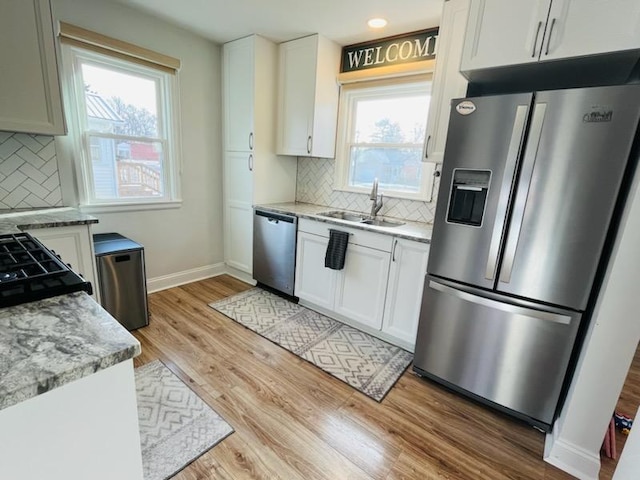 kitchen with a sink, light wood finished floors, white cabinetry, appliances with stainless steel finishes, and baseboards