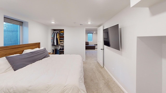 bedroom with baseboards, recessed lighting, multiple windows, a walk in closet, and light colored carpet