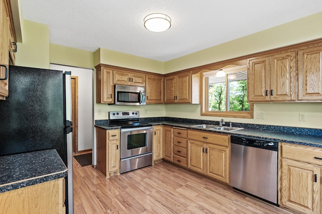 13838 Glendale Trl, Savage, MN 55378 - kitchen with appliances with stainless steel finishes, a sink, light wood-style floors, dark countertops, and a textured ceiling