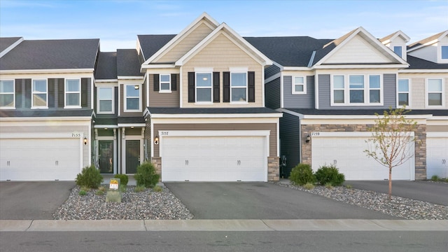 townhome / multi-family property featuring an attached garage, stone siding, and aphalt driveway