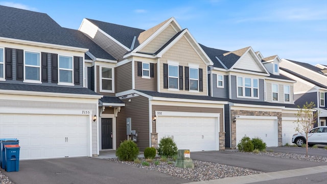 townhome / multi-family property with a garage, driveway, and stone siding