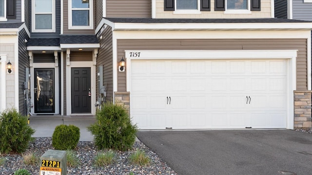 property entrance with driveway, stone siding, and a garage