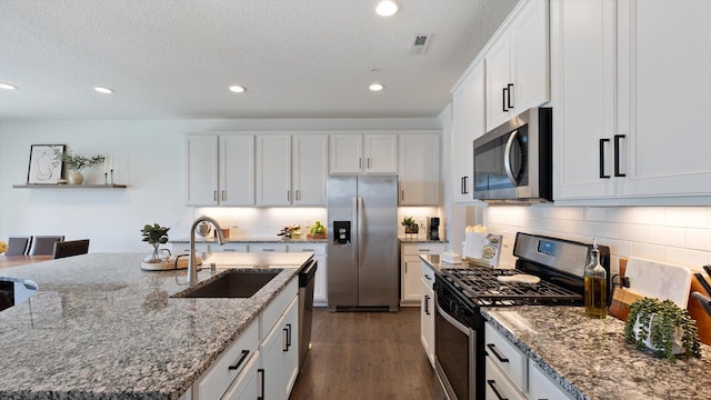 kitchen featuring appliances with stainless steel finishes, tasteful backsplash, a sink, white cabinets, and stone countertops