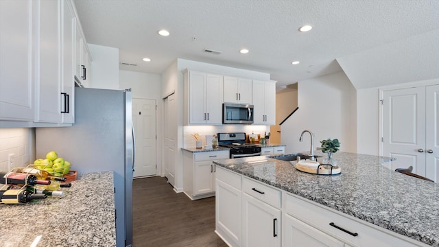 kitchen with white cabinets, light stone counters, a sink, dark wood finished floors, and appliances with stainless steel finishes