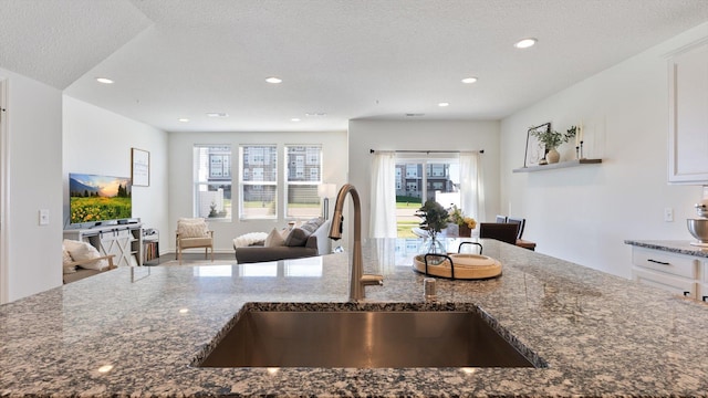 kitchen featuring a sink, dark stone counters, white cabinetry, open floor plan, and recessed lighting